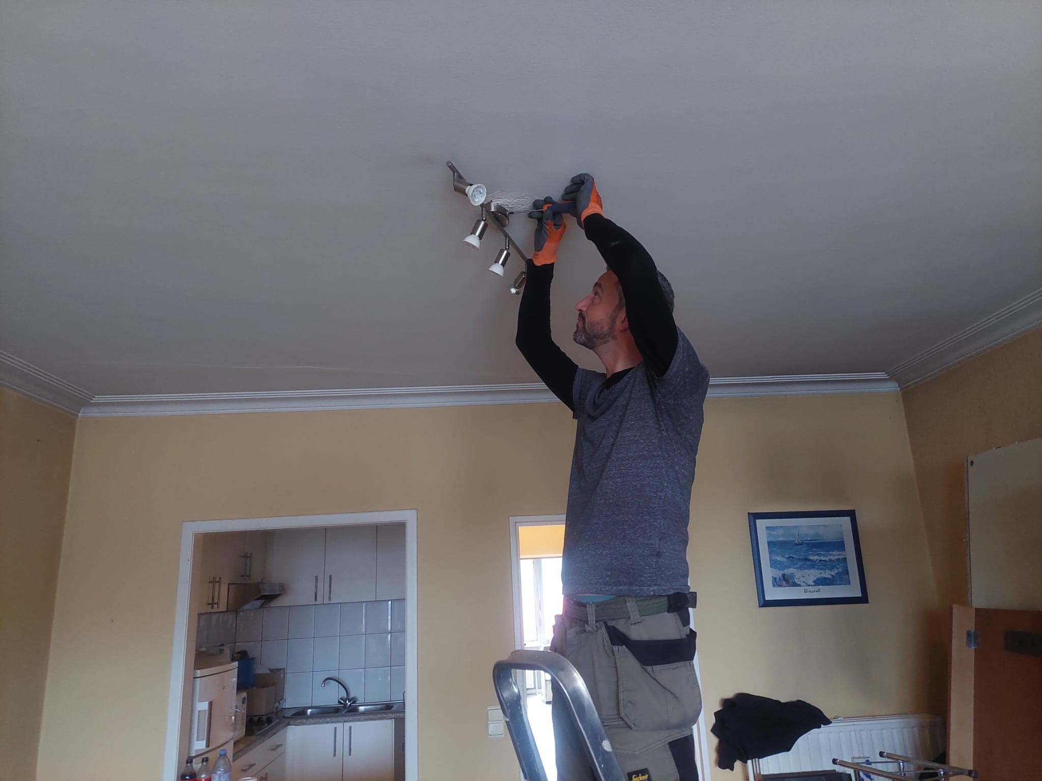 Medewerker van Huisopruimers demonteert een plafondlamp op een ladder tijdens een ontruiming